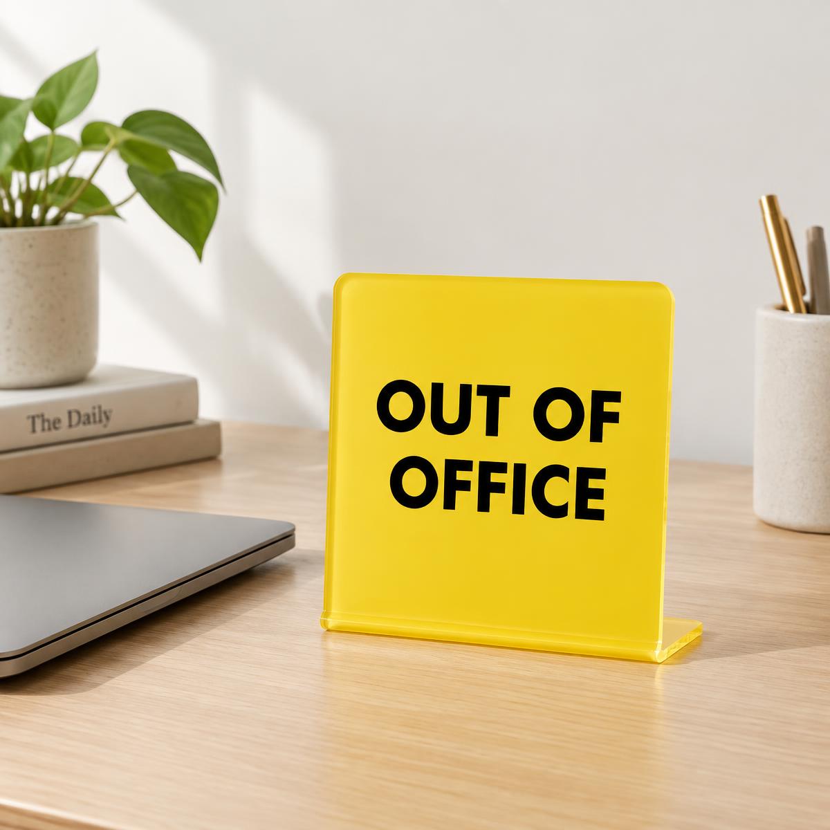 'Out of Office' yellow desk sign standing on a pale oak desk